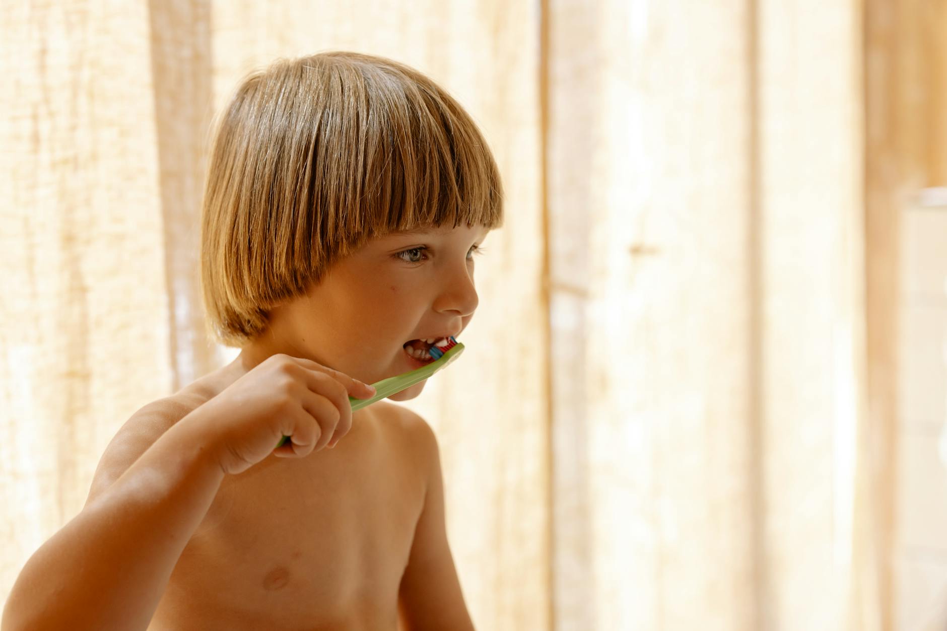 Young boy brushing teeth indoors in soft natural light, promoting dental care routines.